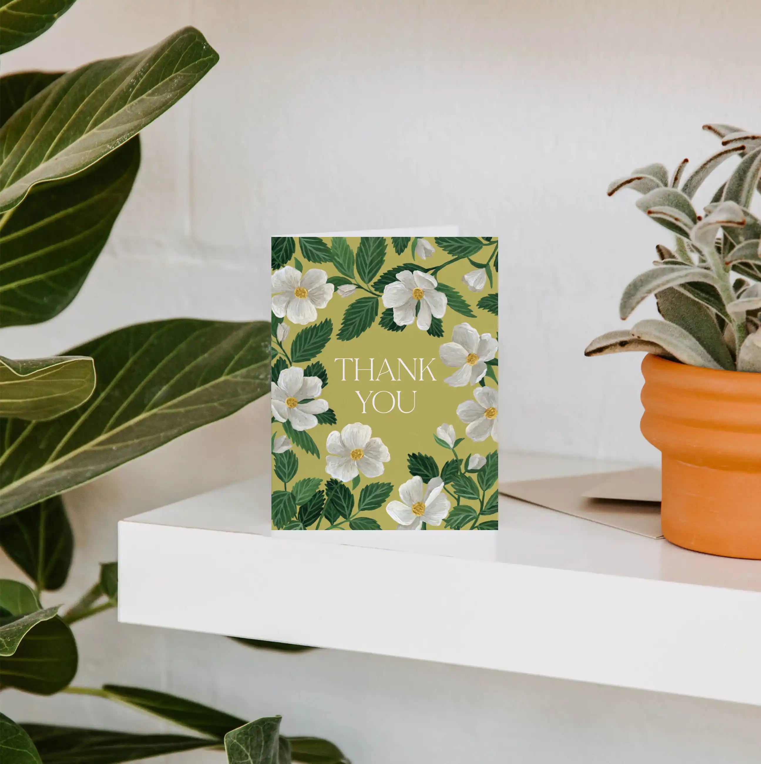 Floral 'Thank You' card on a white surface with plants in the background